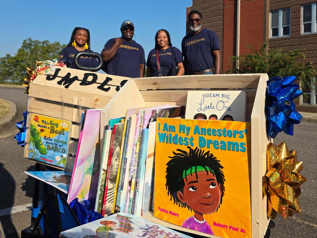 JMDLS members smile behind a display of books collected for donation to local classrooms