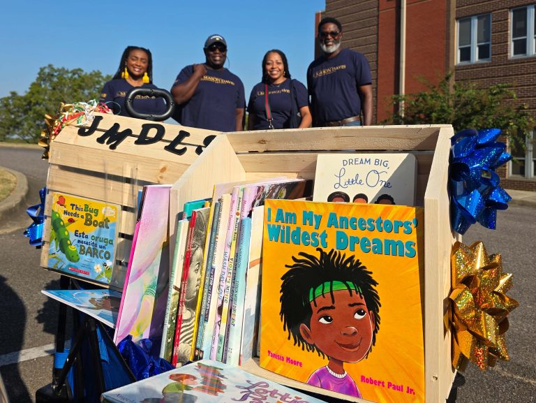 JMDLS members smile behind a display of books collected for donation to local classrooms