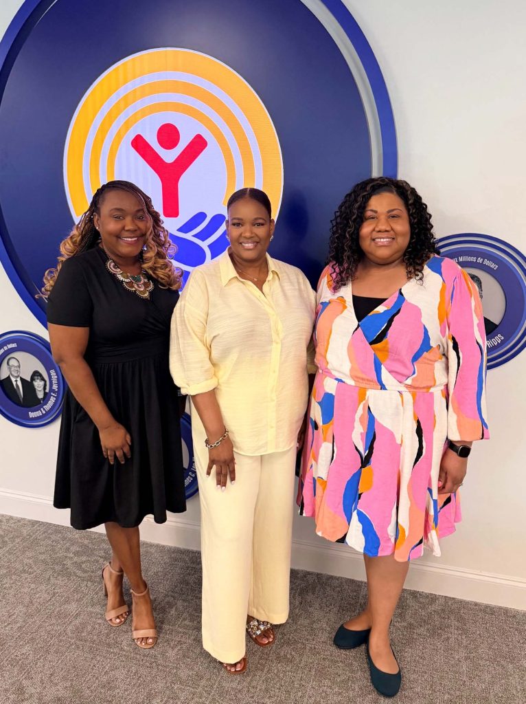 Three Visiting Allocation Team chairs smile together in front of a United Way display during a training event.