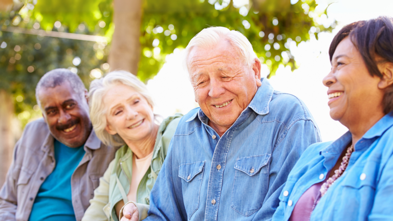four people with silver hair sit outdoors laughing and talking