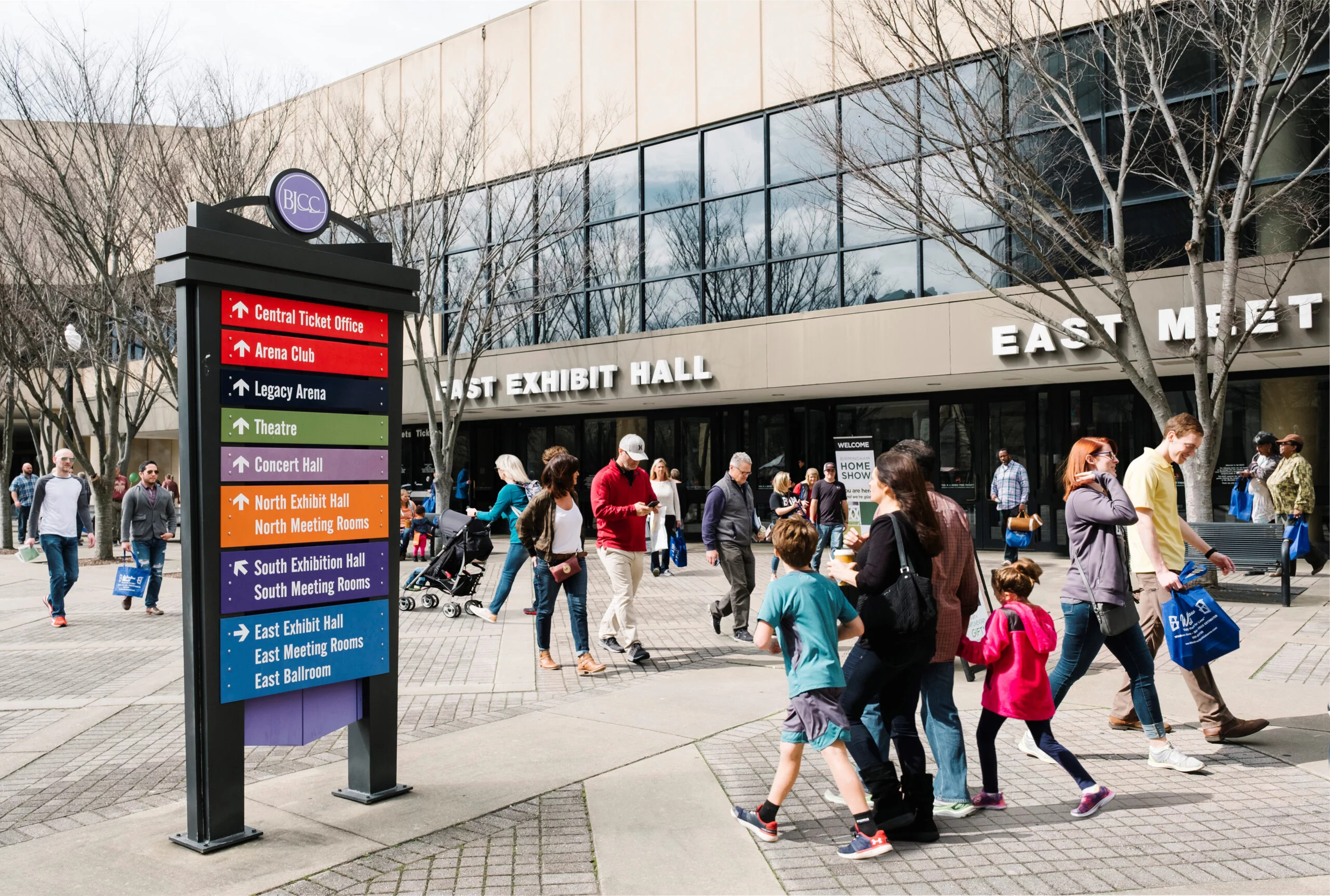 Visitors outside the BJCC East Exhibit Hall near a colorful directional sign.
