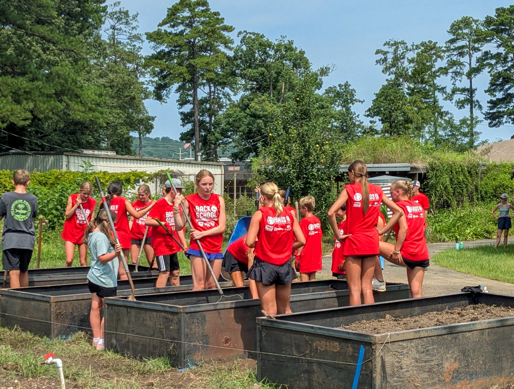 Volunteers wearing Back to School Day of Action shirts work together in raised garden beds during a community service project.