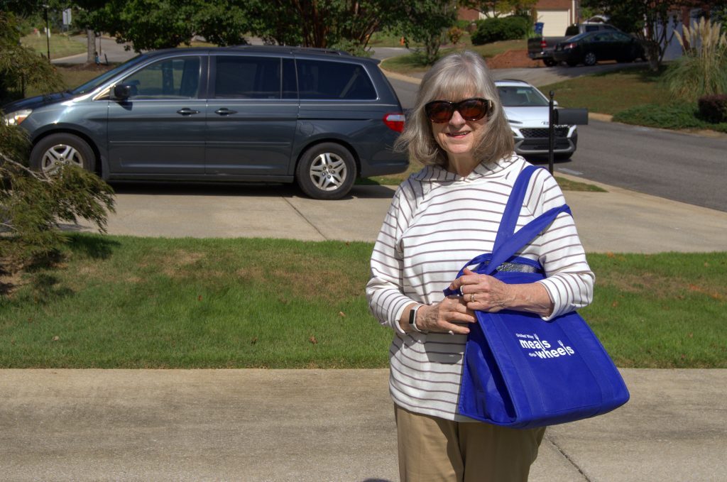 A meals on wheels volunteer walks from her vehicle to a client's home with a meal delivery