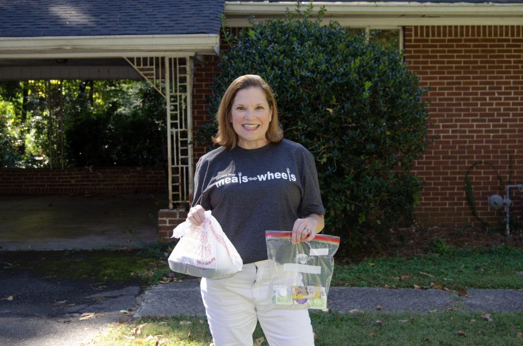 Meals on Wheels volunteer smiles while delivering a meal and care package to a home.