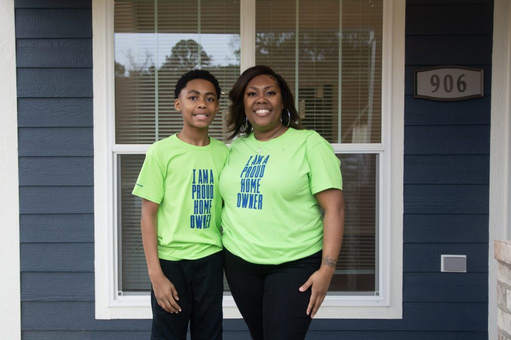 Latifah Leatherwood stands outside her newly completed Habitat for Humanity home in Central Alabama, holding her keys and smiling beside a “Sold” sign bearing her family name, representing her journey to affordable homeownership through community support and partnership.