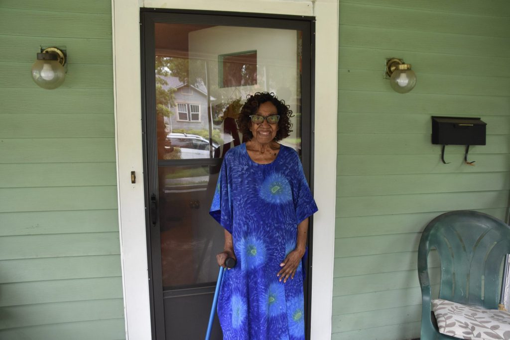Meals on Wheels client Margaret Mitchell smiles at the front door of her Birmingham home while holding a cane.
