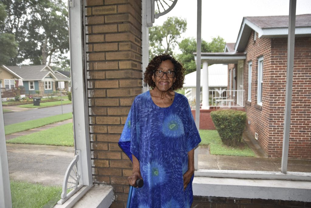 Margaret Mitchell stands on her screened front porch in Birmingham, smiling and holding a cane.