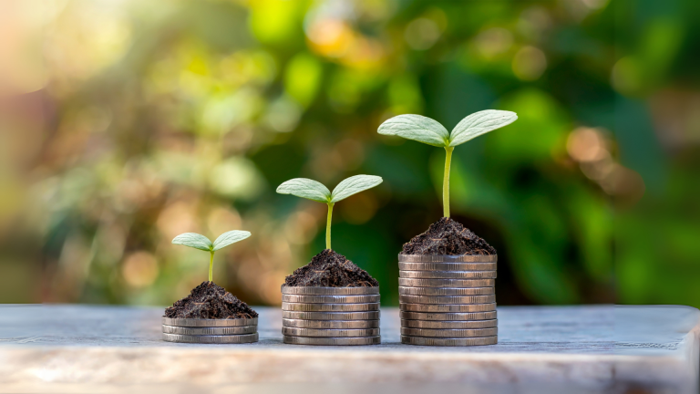 Three stacks of coins with growing plants sprouting from soil on top, symbolizing the increasing impact of matched charitable donations.