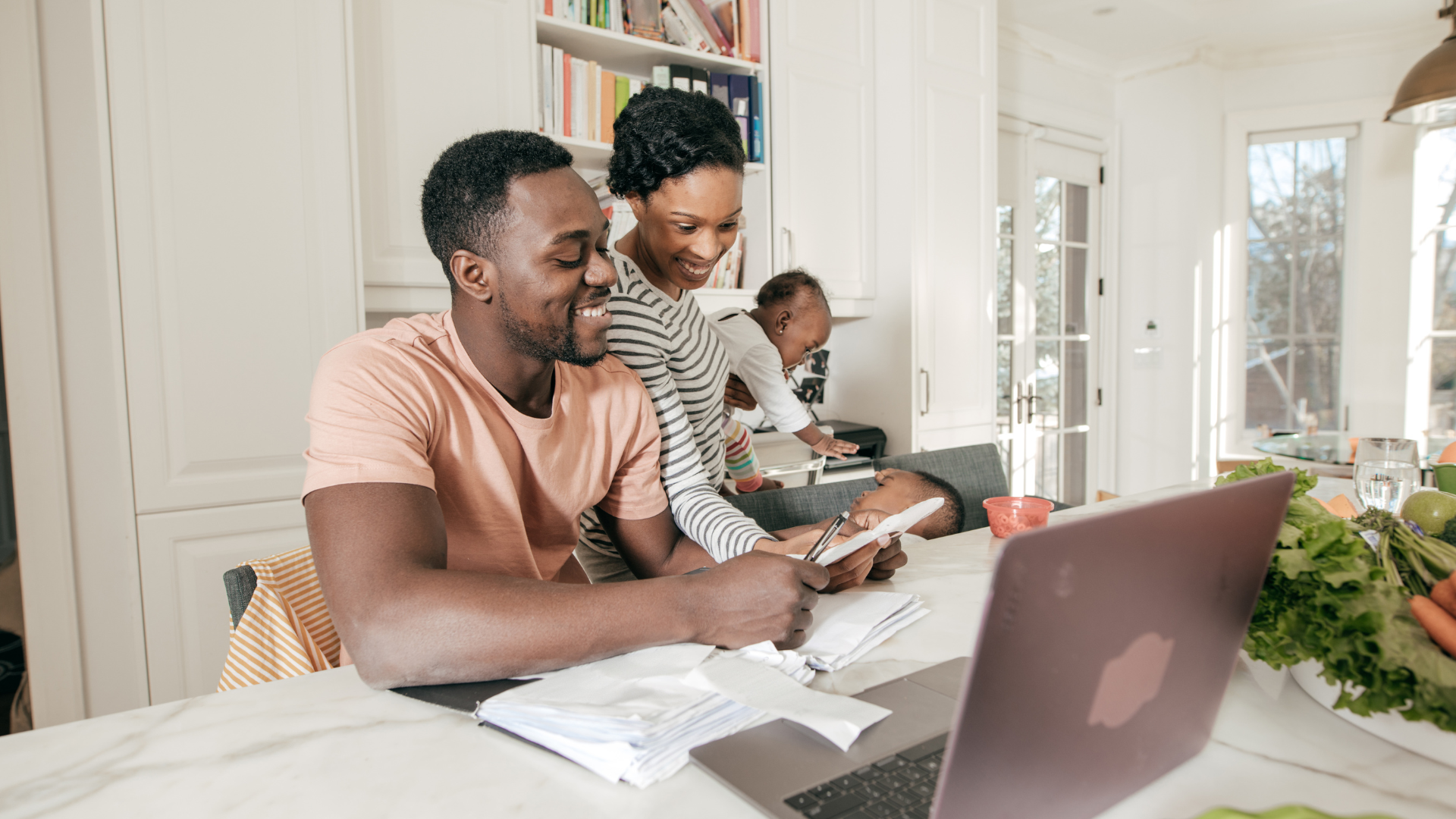 a family sits together at home in a kitchen with financial paperwork and a laptop