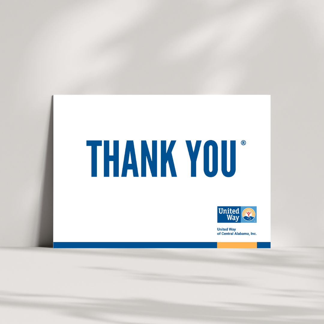 A white thank you card with bold blue text reading “THANK YOU” centered on the front. The United Way of Central Alabama logo appears in the bottom right corner, above a blue and gold accent bar. The card is propped upright with soft shadows in the background.