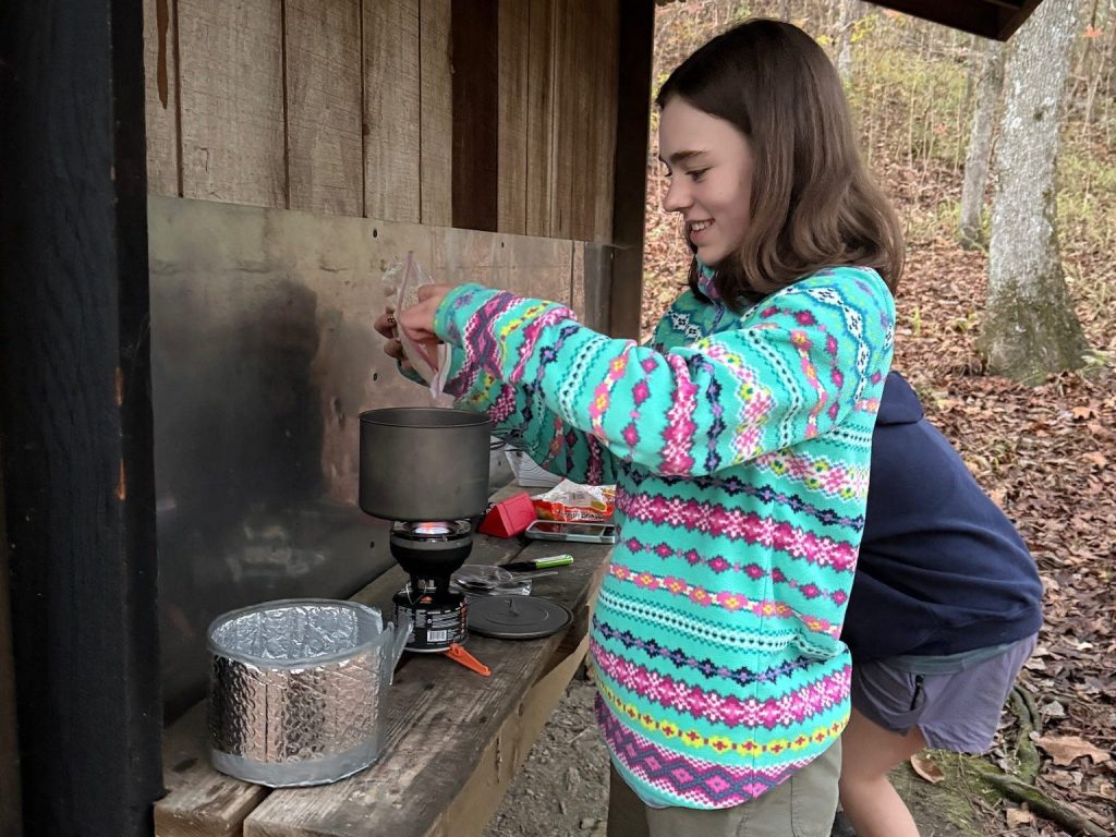 Featured image: Eagle Scout Isabelle Dionne prepares a meal on a camp stove during a Scouting trip. Repeated body image: Leave the alt text empty because the photo duplicates the featured image. Construction image: Three Scouts work together to build a wooden structure using hand and power tools. Outdoor skills image: Isabelle Dionne and other Scouts use a two-person crosscut saw during an outdoor skills activity.