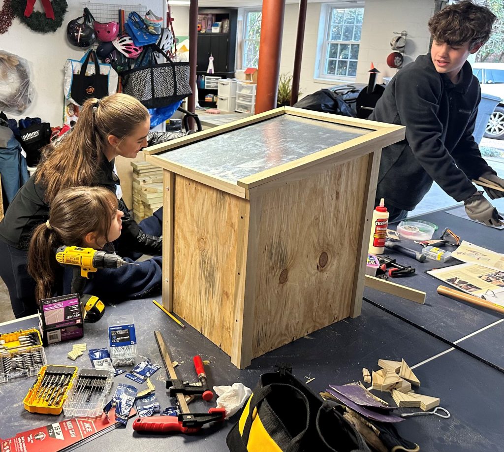 Three Scouts work together to build a wooden structure using hand and power tools.