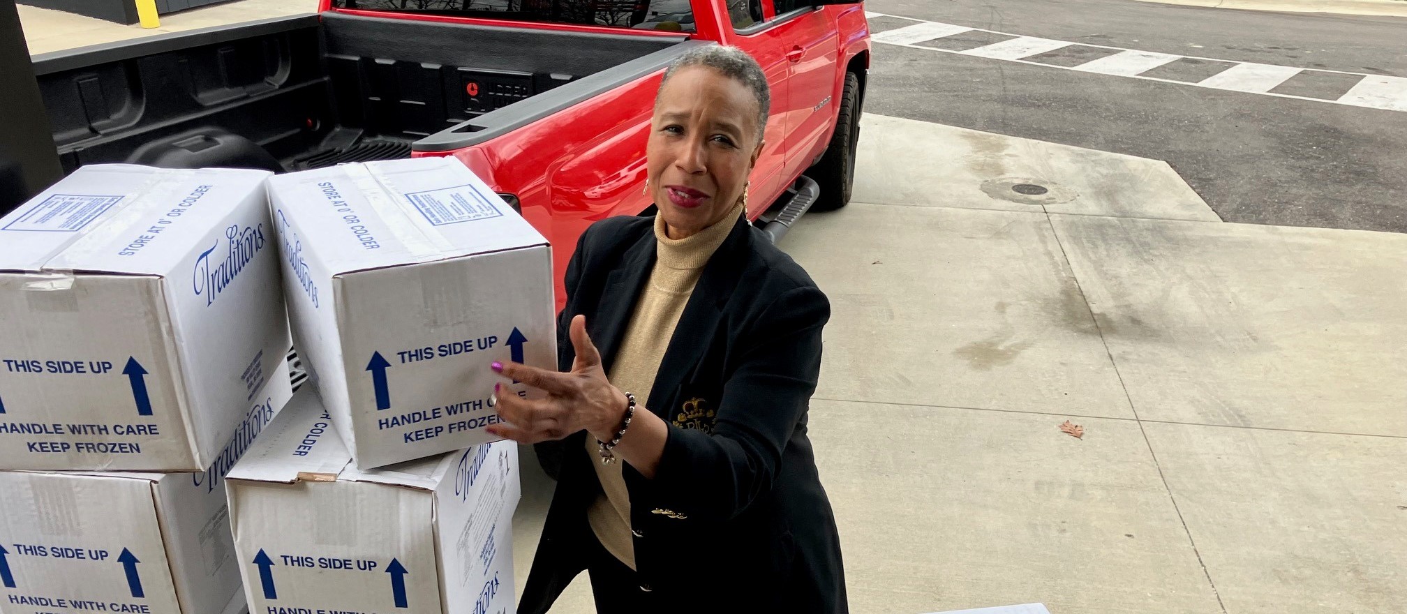 Meals on Wheels team member loading boxes of meals beside a red pickup truck.