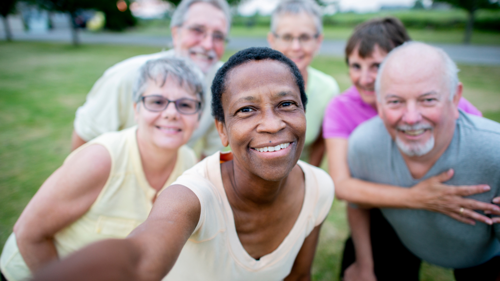 A group of smiling older adults gathers closely outdoors for a cheerful selfie, showcasing friendship and community connection.