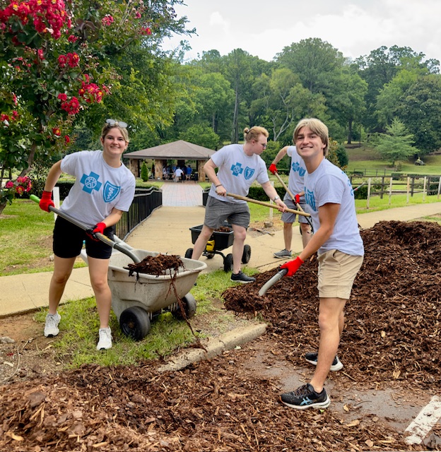 smiling volunteers shovel wheelbarrows full of mulch at a community park